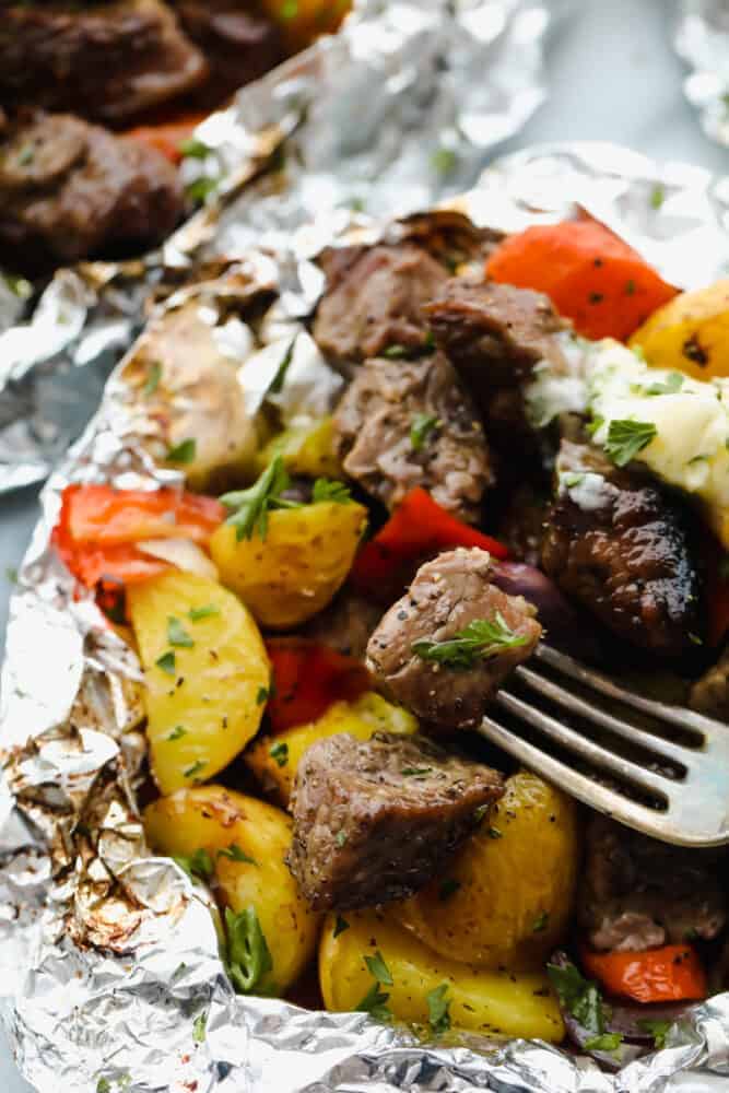 Butter Garlic Herb Steak Foil Packets have melt in your mouth beef with hearty veggies that are grilled to perfection with butter that has garlic and herbs inside. This is one amazing meal that you don't want to miss out on! Steak foil packets opened with a fork in a steak.