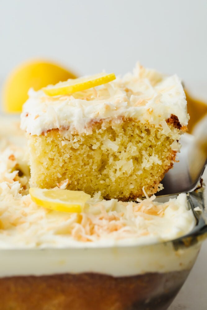 Lemon coconut cake is the perfect combination of delicious flavors and a soft texture! Moist and topped with the flaked coconut, this cake is insanely delicious and SOO good! A slice of lemon coconut cake being sliced and taken out of the pan.