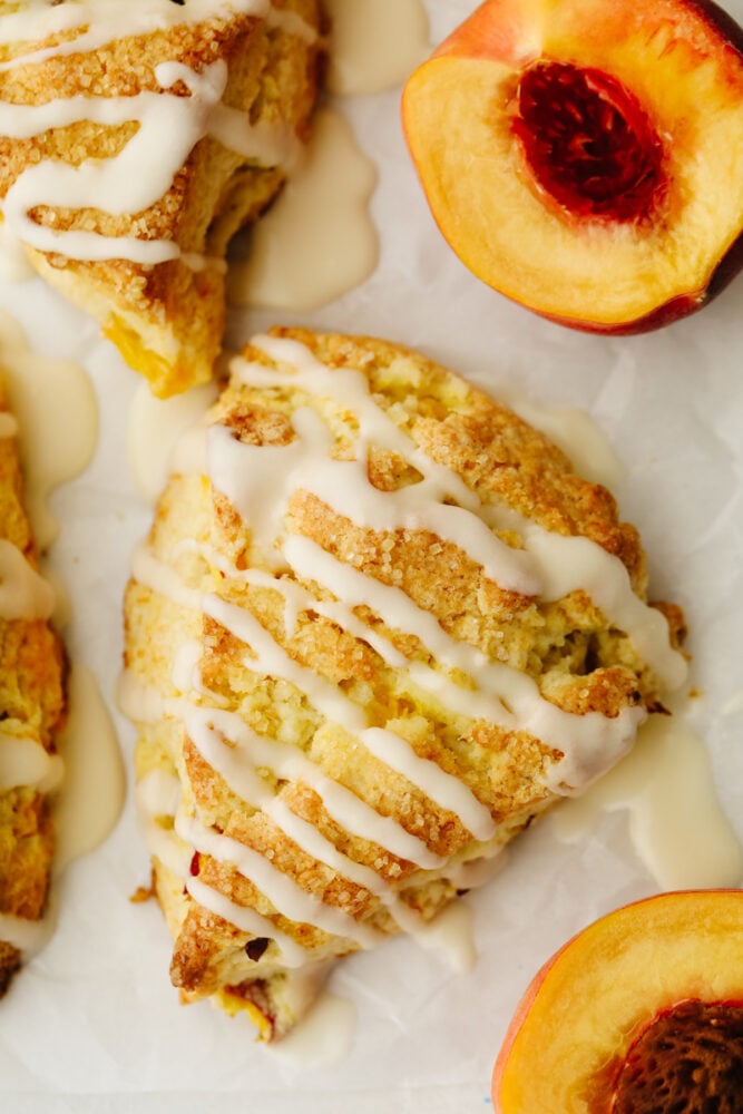 Peach Scones are quite literally summer wrapped in a flakey buttery tender scone. Super ripe sweet peaches are the star of these treats, topped with a sweet vanilla glaze! Up close picture of a peach scone with vanilla icing.