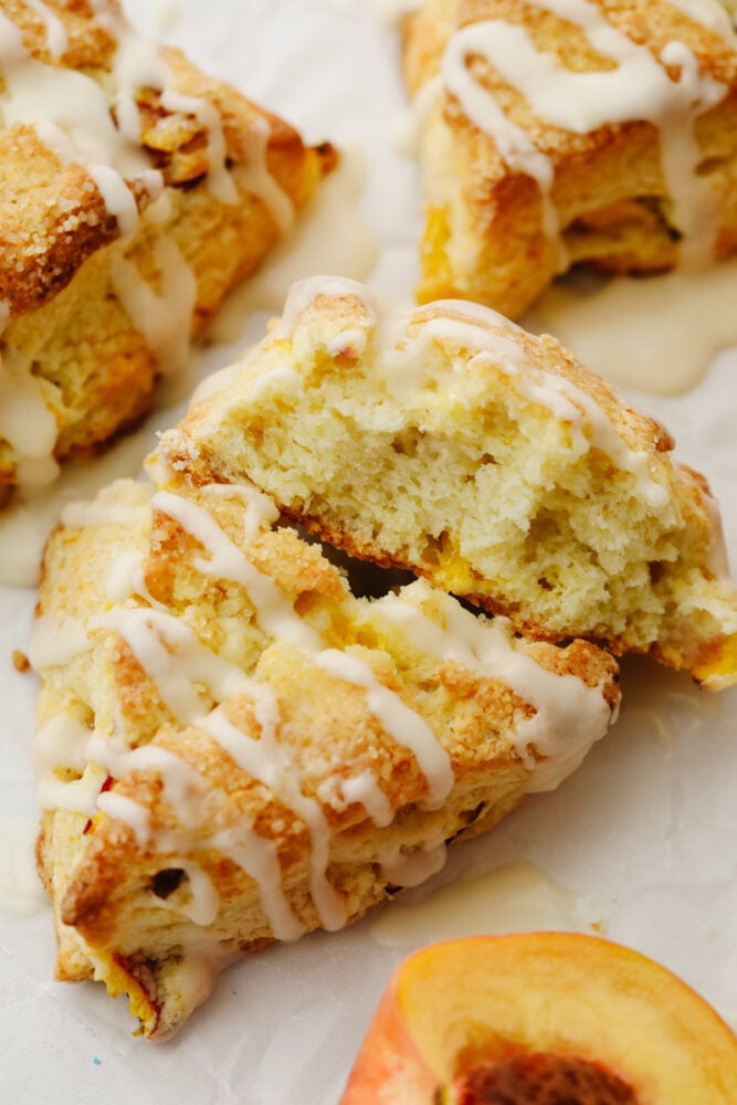Peach Scones are quite literally summer wrapped in a flakey buttery tender scone. Super ripe sweet peaches are the star of these treats, topped with a sweet vanilla glaze! A scone broken in half so you can see the fluffy inside.