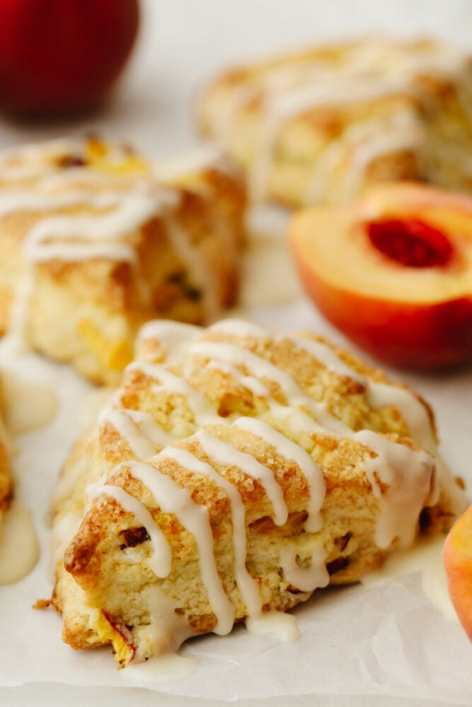Peach Scones are quite literally summer wrapped in a flakey buttery tender scone. Super ripe sweet peaches are the star of these treats, topped with a sweet vanilla glaze! A glazed peach scone topped with crystal sugar.