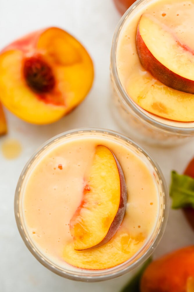 Peach smoothie perfection starts here! It’s fresh, juicy, and extra creamy thanks to Greek yogurt. And a protein boost to power you through your busy morning. Topview of a peach smoothie with a peach garnishing the top.