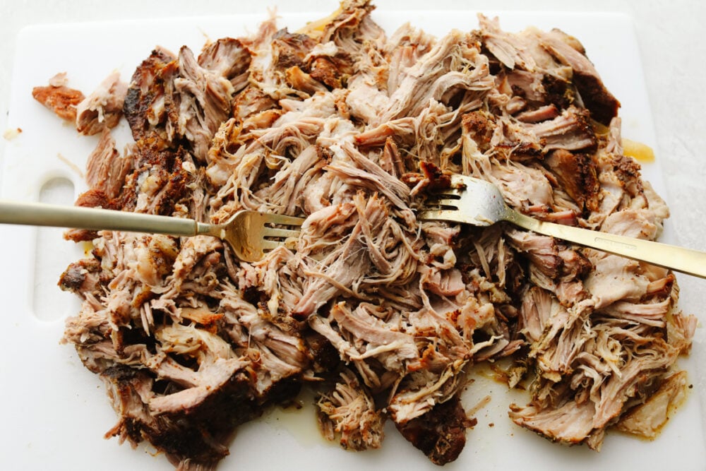 Pork carnitas tacos are mouthwatering, juicy, and insanely delicious! They will satisfy even the pickiest of eaters and everyone will keep coming back for more! Pork being shredded with two forks.