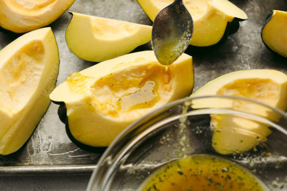 Roasted parmesan acorn squash is deliciously smooth and loaded with flavor! Mixed with these amazing spices, once this is cooked up, you will have found your own little slice of heaven! Oil and spices being drizzled on squash with a spoon.