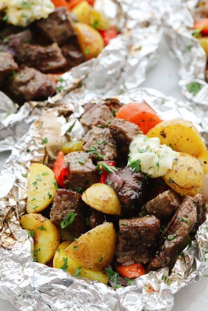 Butter Garlic Herb Steak Foil Packets have melt in your mouth beef with hearty veggies that are grilled to perfection with butter that has garlic and herbs inside. This is one amazing meal that you don't want to miss out on! Close up of steak and vegetables in foil.