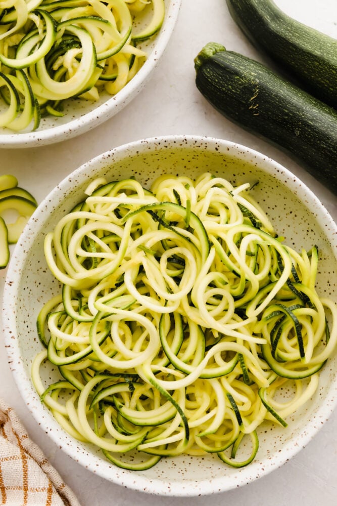 Zucchini noodles are the perfect low-carb option for pasta night. Use these 3 cooking methods to add a little healthy goodness to dinnertime! Raw grated zucchini in a bowl.