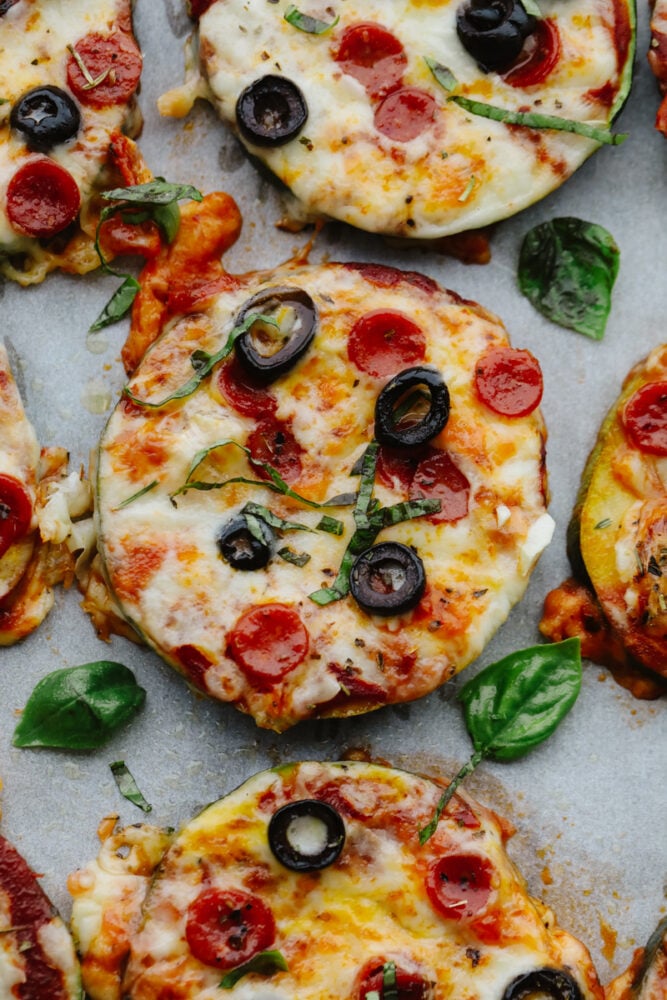 These melty, cheesy zucchini pizza bites have all the goodness of pizza without the carbs! In just 15 minutes, you have a tasty appetizer that you can feel great about eating! Close-up of zucchini pizza bites with basil garnish.