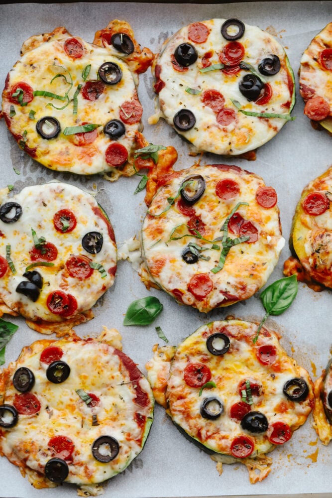 These melty, cheesy zucchini pizza bites have all the goodness of pizza without the carbs! In just 15 minutes, you have a tasty appetizer that you can feel great about eating! Zucchini pizza bites on a baking sheet lined with parchment paper.