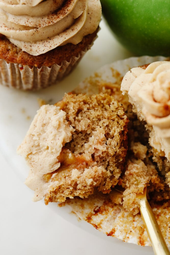 Apple pie cupcakes are a twist on a classic dessert. They are moist, delicious and with fresh apple pie filling in the middle, they give you JUST the right amount of texture! An apple pie cupcake being cut into with a fork.