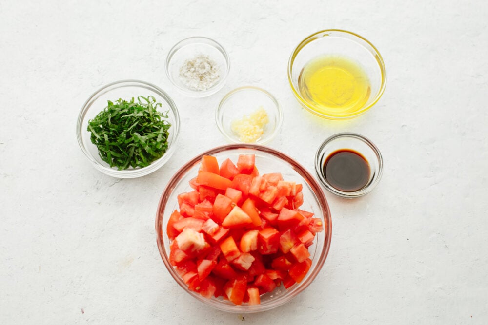 Showcase fresh tomatoes with this light and refreshing tomato basil salad! It's tossed with aromatic herbs, olive oil, and vinegar for fresh, bright flavor that is hard to resist! Bowls of chopped tomatoes and vinaigrette ingredients.