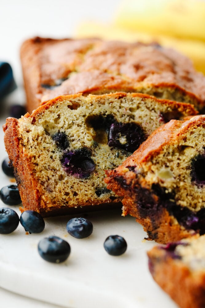 This staple blueberry banana bread recipe has the perfect combination of bananas and fresh blueberries. It is so moist, delicious, andย super simple to make! Closeup of blueberry banana bread slices.