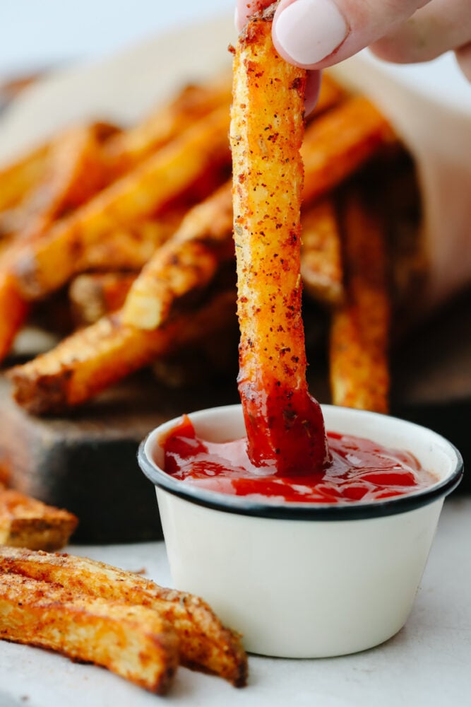 Cajun fries are baked to absolute perfection! With a delicious, spicy taste and crispy texture, I don't think that they get much better than this! A cajun fry being dipped in ketchup.