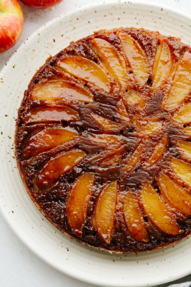Caramel apple upside-down cake is just the dessert you need for fall! It's rich, moist, and smothered in a scrumptious caramel glaze! A full caramel apple upside-down cake on a white serving dish.