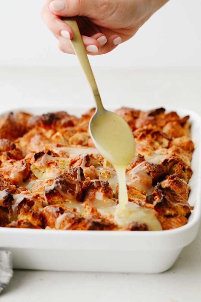 Croissant bread pudding is the perfect breakfast food! Drizzled with a creamy, vanilla sauce, this soft bread pudding is so amazing that you won't want to stop at just one piece! Vanilla sauce being drizzled on croissant bread pudding.