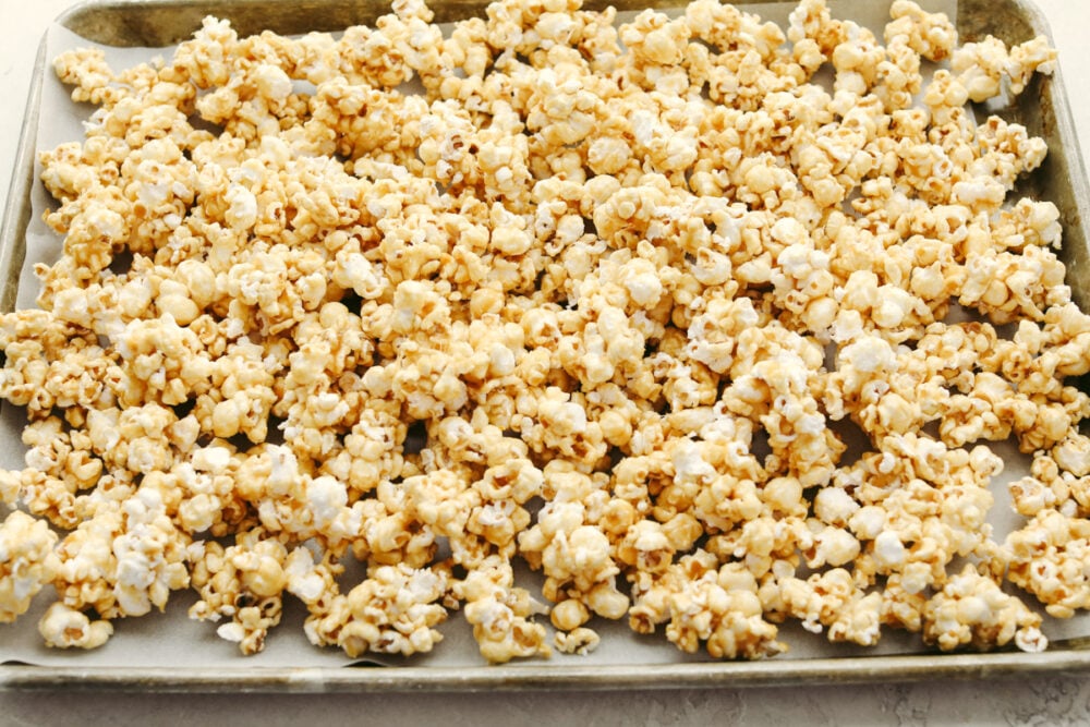 Crunchy caramel corn is absolutely divine! This classic crunchy snack delivers on that deep, rich caramel flavor that we all know and love! Eat it at home or on the go...Either way, you're going to be hooked! Caramel corn on a cookie sheet.