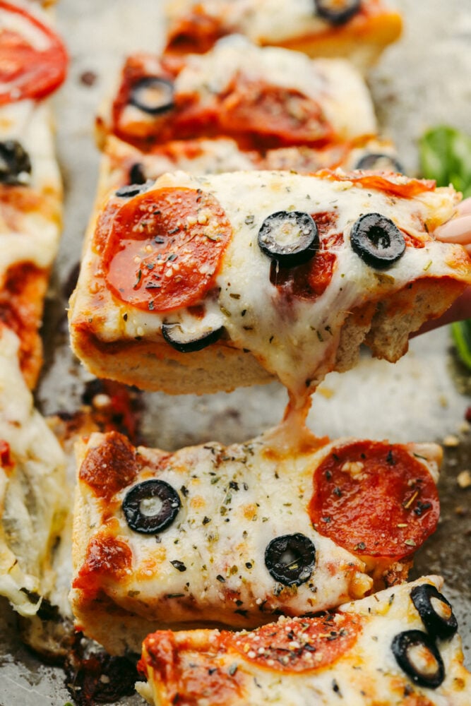 French bread pizza is quick, easy, AND delicious! Topped with all of your favorite things, this simple pizza delivers amazing taste! It's definitely a winner! Someone picking up a slice of pizza to eat.