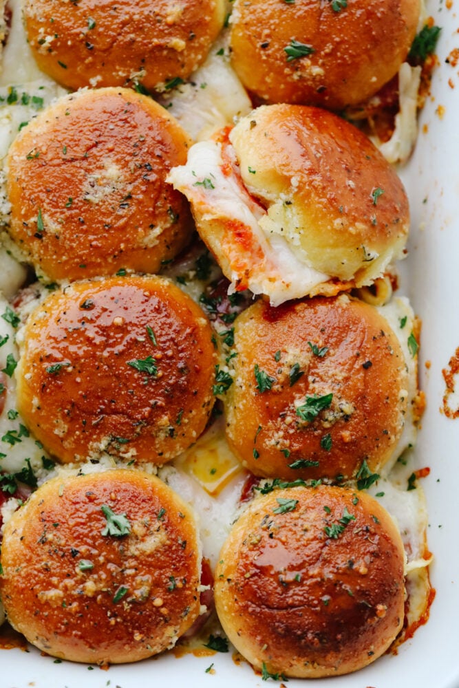 These pizza sliders are about to become your new favorite appetizer. Brushed with a buttery Italian seasoning glaze and filled with all of your favorite pizza toppings, each bite is truly irresistible! A top-down view of 8 pizza sliders.