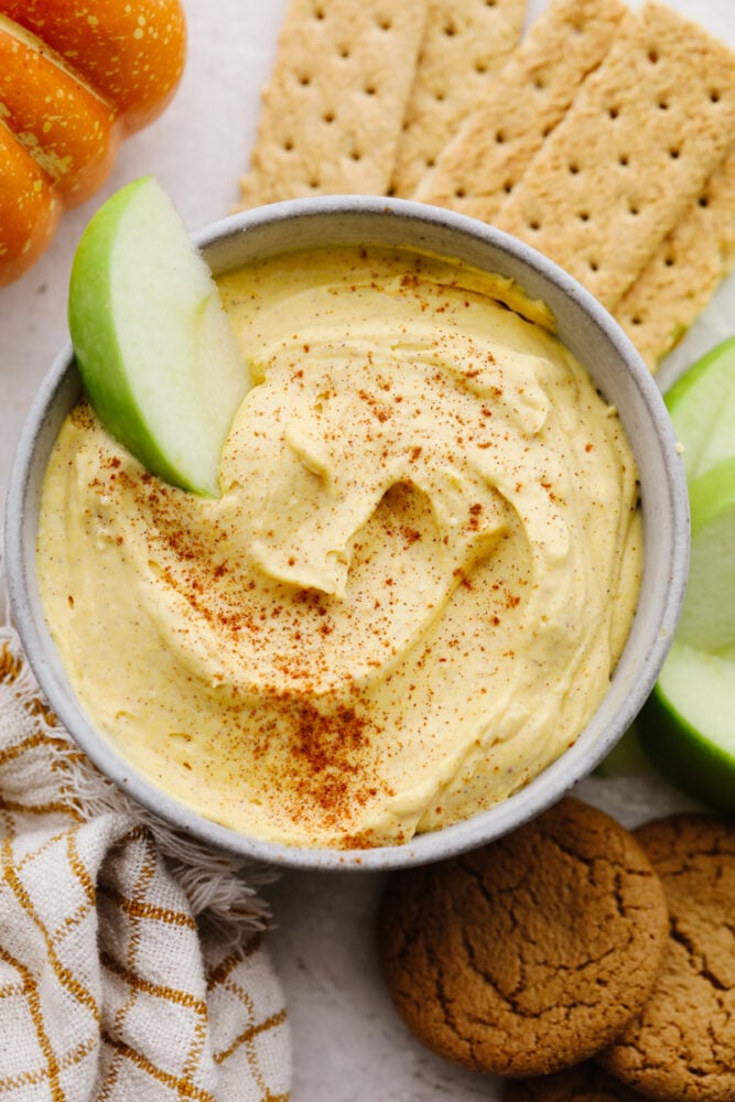 Pumpkin pie dip is deliciously light and fluffy! It has to creamiest texture and the spices bring that pumpkin pie flavor to life! It is something that your whole family will go crazy over!ย Pumpkin pie dip in a bowl with an apple slice in it.