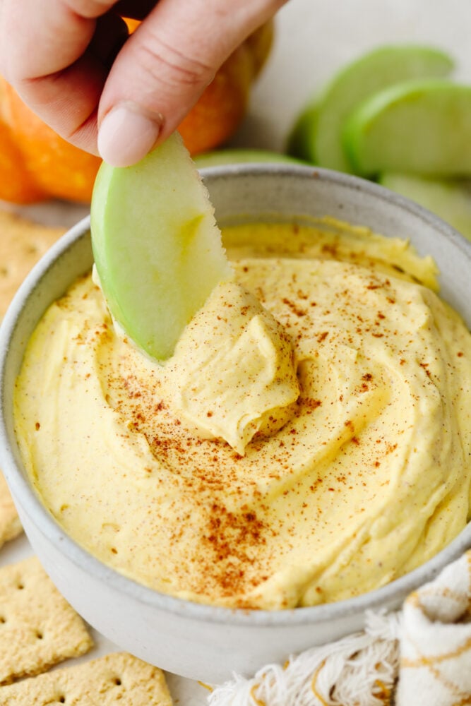 Pumpkin pie dip is deliciously light and fluffy! It has to creamiest texture and the spices bring that pumpkin pie flavor to life! It is something that your whole family will go crazy over!ย Someone dipping an apple into pumpkin pie dip.