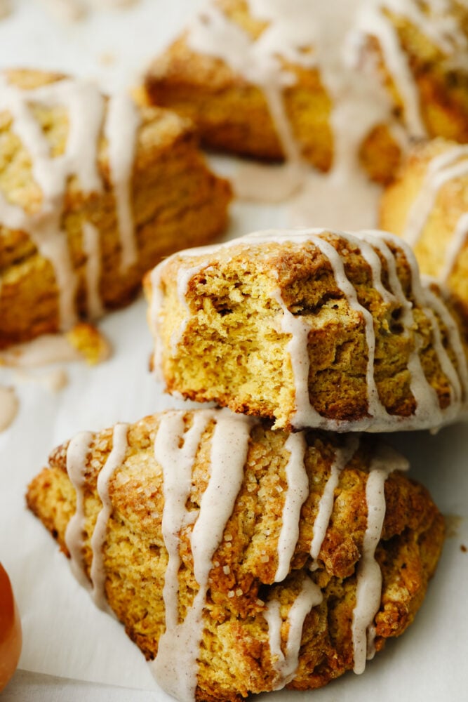 Pumpkin scones are absolutely mouthwatering and delicious! Filled with pumpkin flavor and drizzled with cinnamon icing, this is a breakfast option that you won't be able to pass up! A scone with a bite taken out of it.