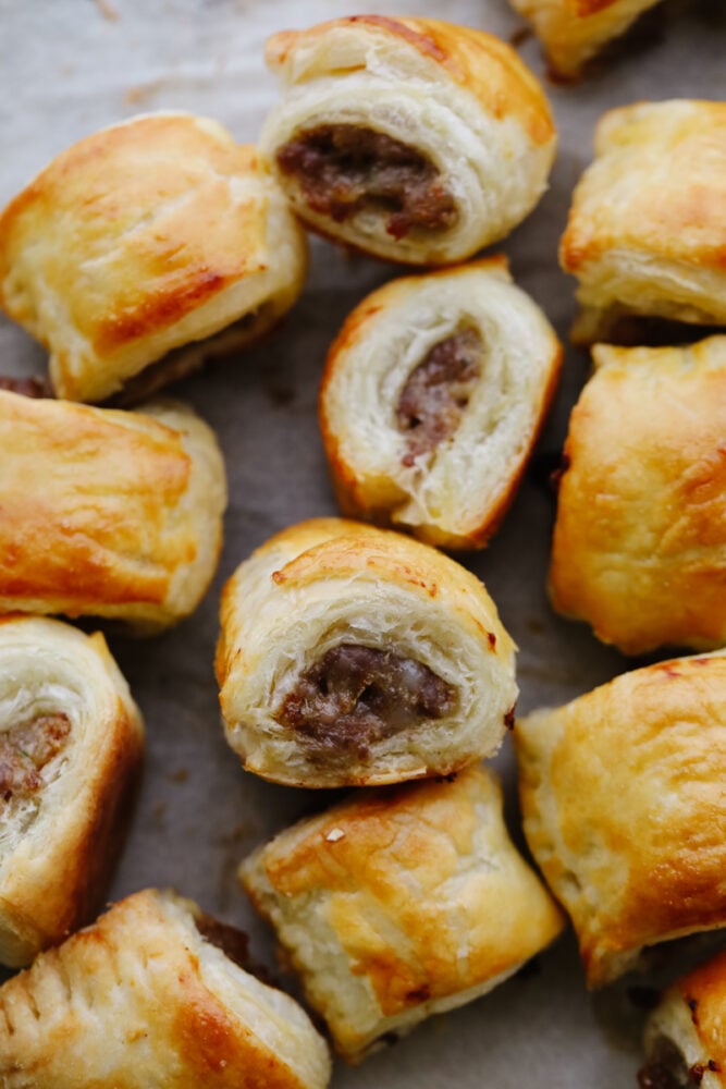 Sausage rolls are perfectly flaky, savory, and absolutely delicious! The best appetizer or snack, these sausage rolls will for sure be a hit among your party guests! A sausage roll on a baking sheet.