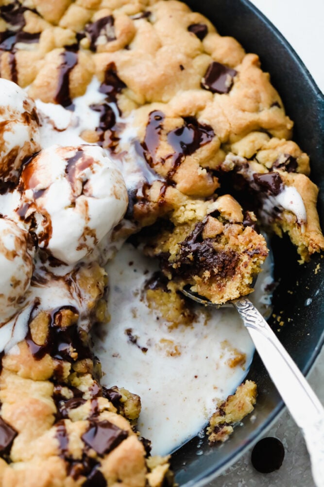This ooey-gooey skillet cookie brings homemade cookies to the next level! It is warm, sweet and the chocolate just melts right in your mouth! You definitely won't be able to stop at just one bite! A skillet cookie being scooped up with a spoon.