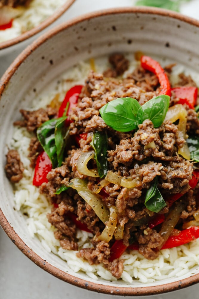 Thai basil beef is simple and delicious! It's made with a homemade Thai sauce that has a bold and brilliant flavor and can be thrown together in less than 30 minutes. It is SOO GOOD! A close up of Thai basil beef on rice, in a bowl.