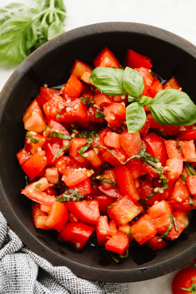 Showcase fresh tomatoes with this light and refreshing tomato basil salad! It's tossed with aromatic herbs, olive oil, and vinegar for fresh, bright flavor that is hard to resist! Tomato basil salad in a brown bowl.