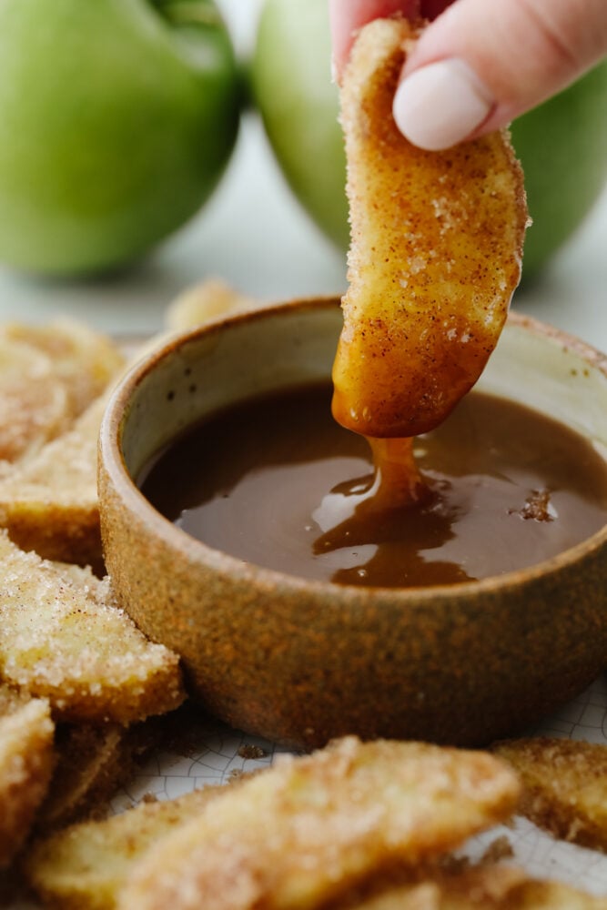 Lightly battered and tender, apple fries are going to become your new favorite treat! A generous coating of cinnamon sugar and homemade caramel dip make them even more irresistible! Dipping apple fry in caramel sauce.