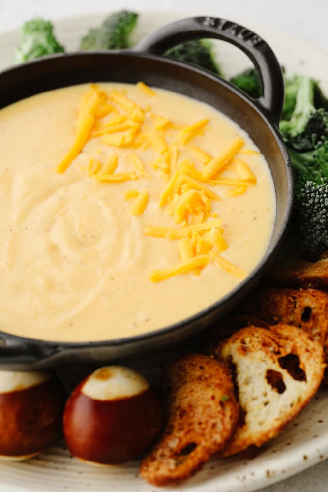 Beer cheese dip is the creamiest, tastiest dip out there! It goes with everything and it's the hit at every party. It has the perfect blend of flavors that will keep you coming back for more! Beer cheese dip on a platter with broccoli, pretzel rolls and a crostini.