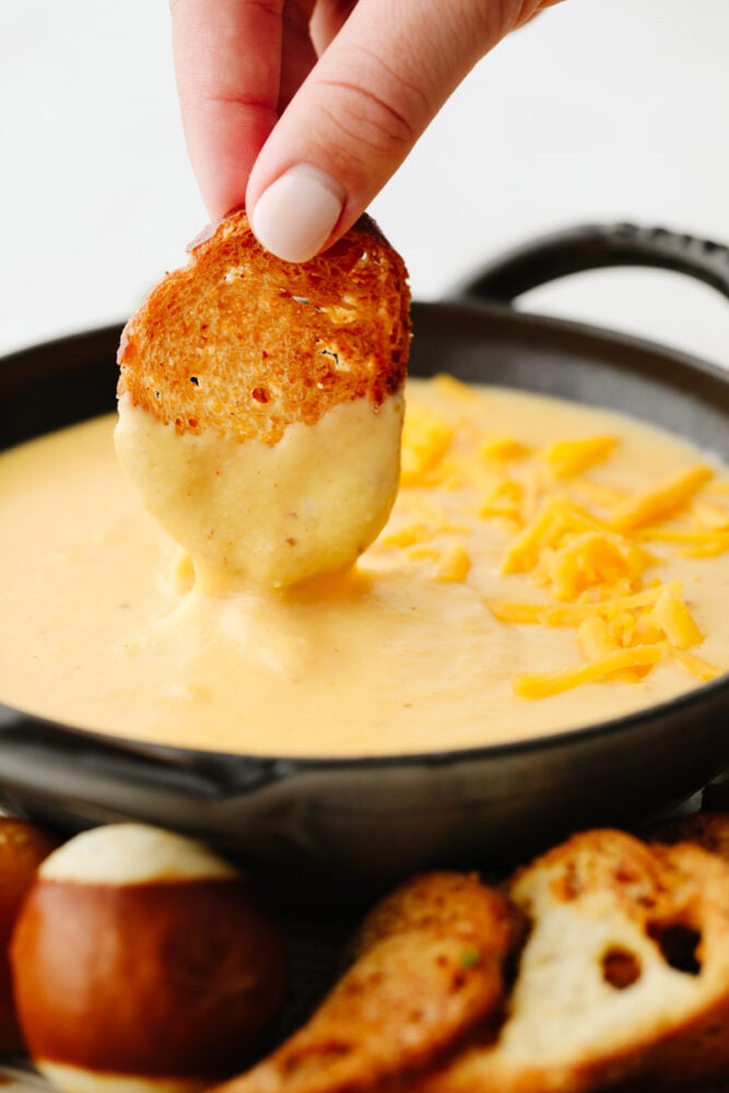 Beer cheese dip is the creamiest, tastiest dip out there! It goes with everything and it's the hit at every party. It has the perfect blend of flavors that will keep you coming back for more! A slice of a crostini being dipped into beer cheese dip.