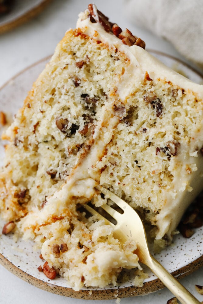 Soft, tender, and filled with nutty goodness, this butter pecan cake is perfect for fall! Browned butter cream cheese frosting and fresh chopped pecans make each bite a dream. Taking a bite of a slice of butter pecan cake.