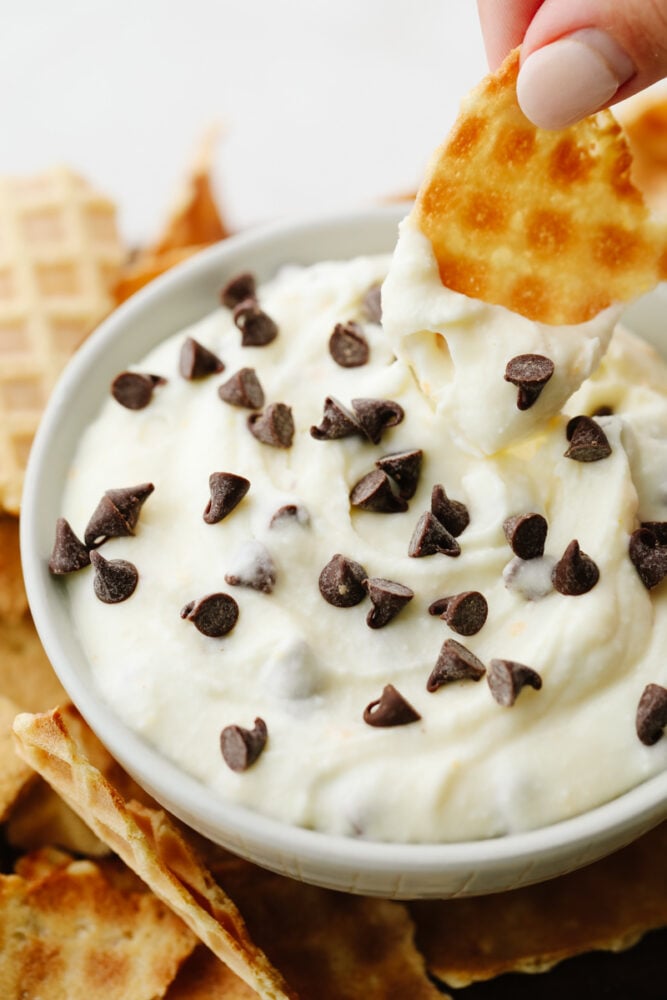 Cannoli dip is amazingly rich and creamy! Dip some broken-up waffle cones into it and you have yourself a delightful dessert! A piece of a waffle cone being dipped into the cannoli dip.