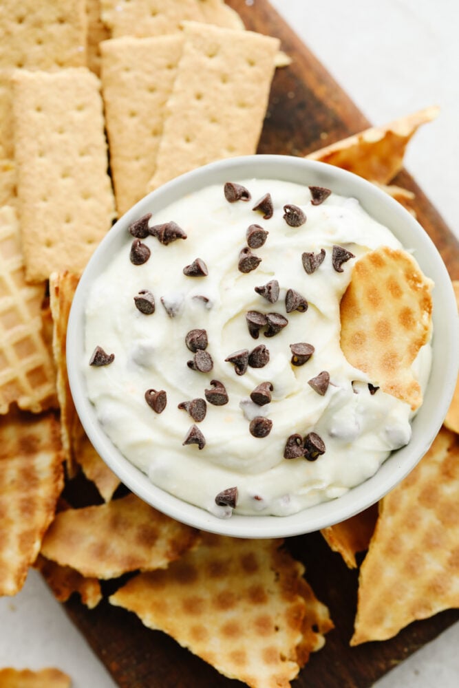 Cannoli dip is amazingly rich and creamy! Dip some broken-up waffle cones into it and you have yourself a delightful dessert! Cannoli dip with mini chocolate chips on a tray with broken up waffle cones and graham crackers.