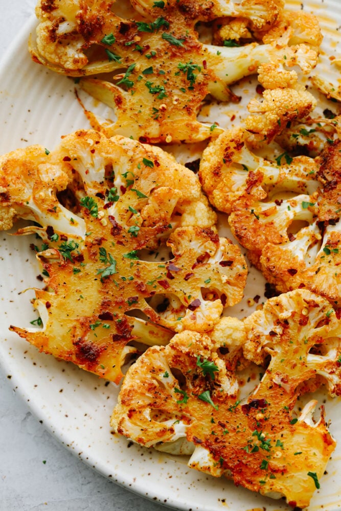 Making roasted cauliflower steaks is the best way to show all this veggie has to offer! They're amazingly tender and tossed in a mouthwatering blend of garlic, paprika, and parmesan. 4 cauliflower steaks on a white plate.