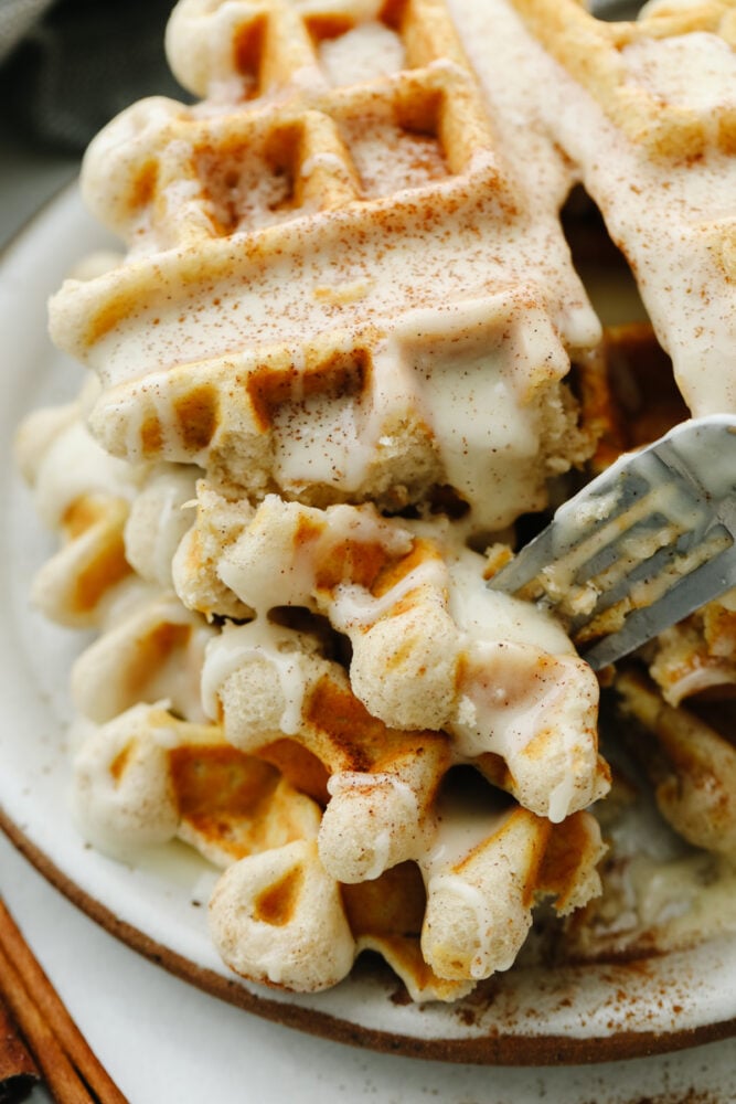 You just can't beat a delicious cinnamon waffle that is drizzled with a cream cheese glaze! It tastes just like a cinnamon roll in waffle form! A cinnamon roll waffle being cut into with a fork.