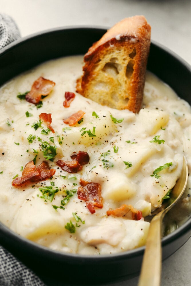 Creamy Clam Chowder with potatoes and vegetables is one of my favorite easy soup recipes! It's thick and creamy and tastes as if it came straight from a restaurant! It's SOO GOOD! A bowl of clam chowder with a spoon and a crostini.