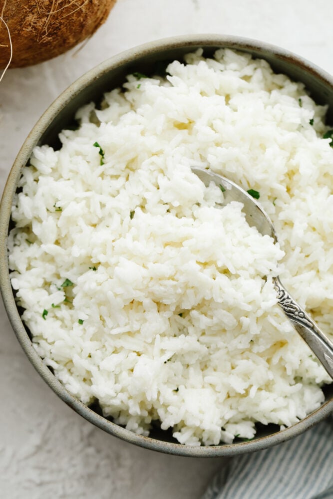 This coconut rice is now going to be one of your go-to side dishes! Fluffed to perfection this rice is SOO GOOD and is super easy to make! Coconut rice in a bowl with cilantro and a spoon.