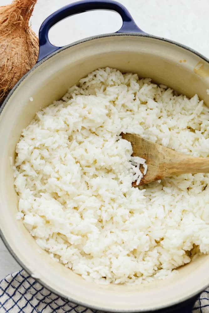 This coconut rice is now going to be one of your go-to side dishes! Fluffed to perfection this rice is SOO GOOD and is super easy to make! Coconut rice in a bowl with a wooden spoon.