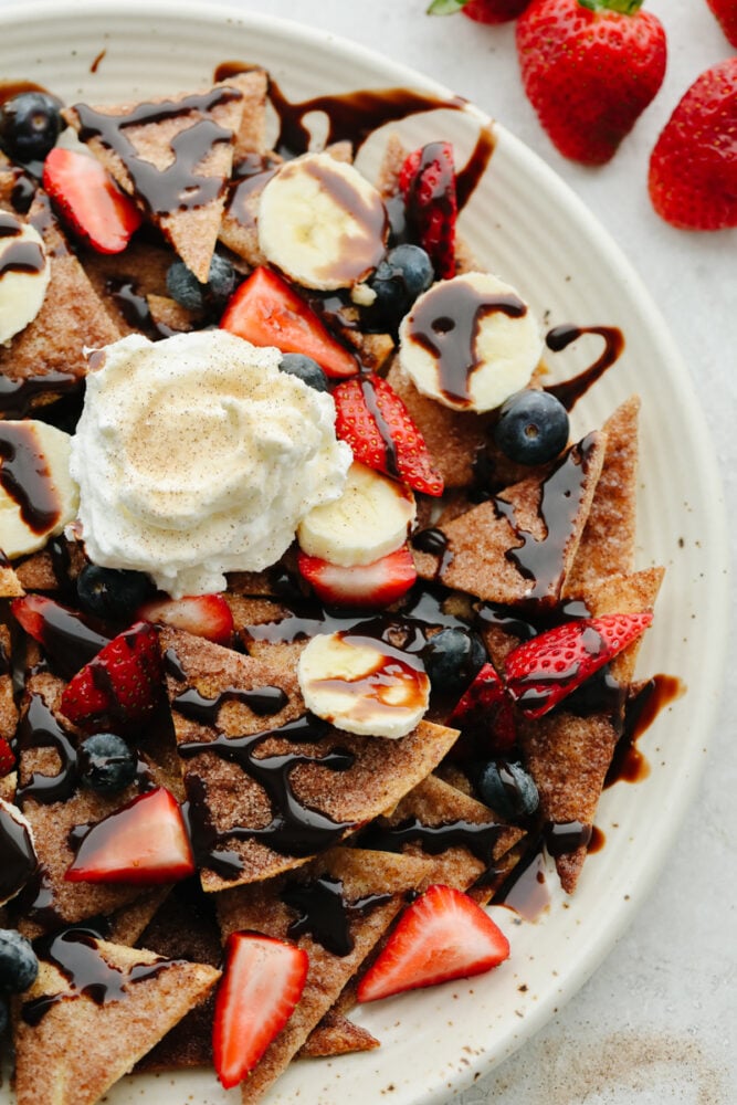These dessert nachos are so delicious! Cinnamon sugar tortilla chips that are topped with fruit, chocolate, and whipped cream. You won't find a dessert more loved than this one! A plate of dessert nachos tipped with whipped cream.