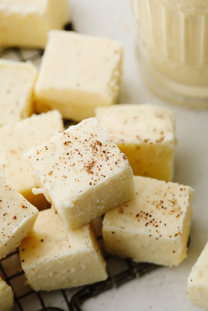 This eggnog fudge is every eggnog lover's dream! Each bite is filled with melt-in-your-mouth white chocolate and dusted with nutmeg! Closeup of eggnog fudge cubes dusted with nutmeg.