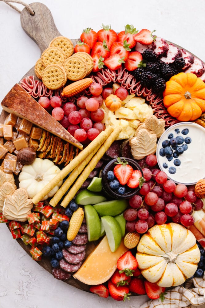 This fall charcuterie board is easy to make and is perfect for all of the parties this season! Packed with colorful and delicious food it is sure to be a hit with all of your guests! A zoomed in pictures of a fall charcuterie board.