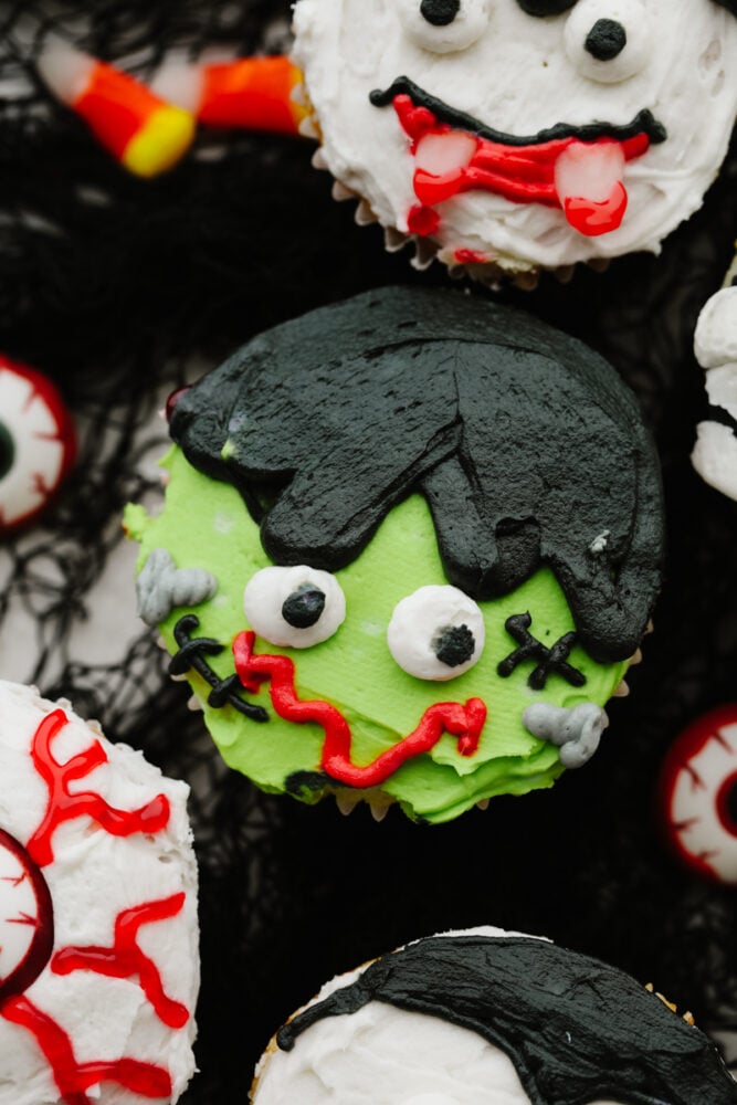 Halloween cupcakes are as tasty as they are cute! Moist vanilla cupcakes are frosted with timeless Halloween characters for an unforgettable treat! Closeup of a Frankenstein cupcake.
