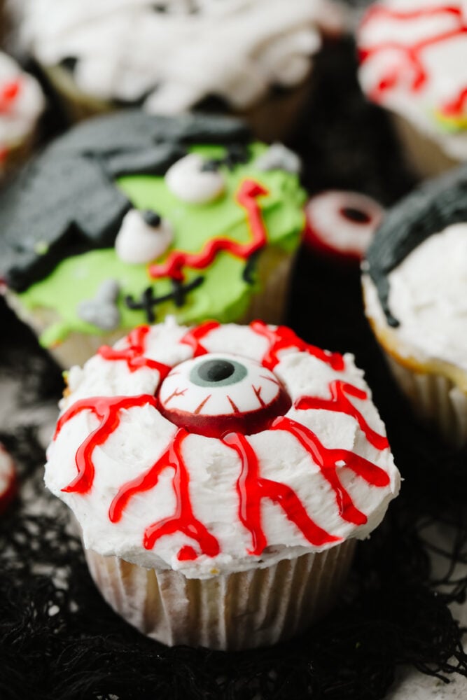 Halloween cupcakes are as tasty as they are cute! Moist vanilla cupcakes are frosted with timeless Halloween characters for an unforgettable treat! Closeup of an eyeball cupcake.