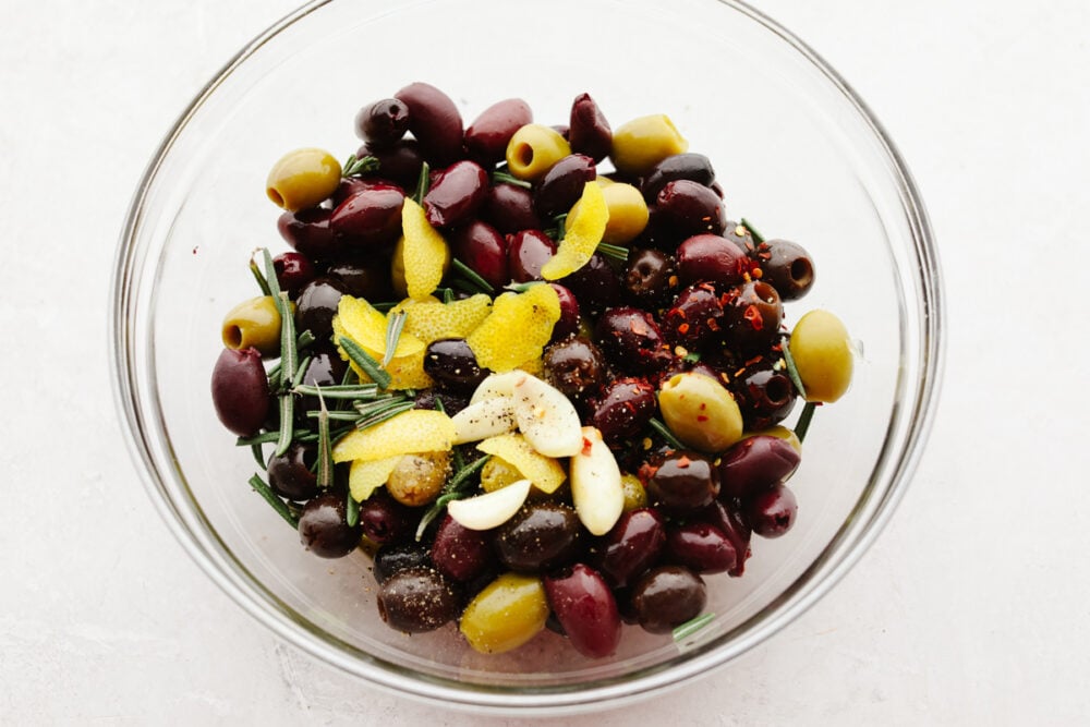 Marinated olives is a fancy appetizer that comes together with little effort and inexpensive ingredients! Meaty, flavorful olives are layered with fresh herbs, spices, and olive oil for an experience your taste buds will absolutely love! A mix of olives topped with seasonings.
