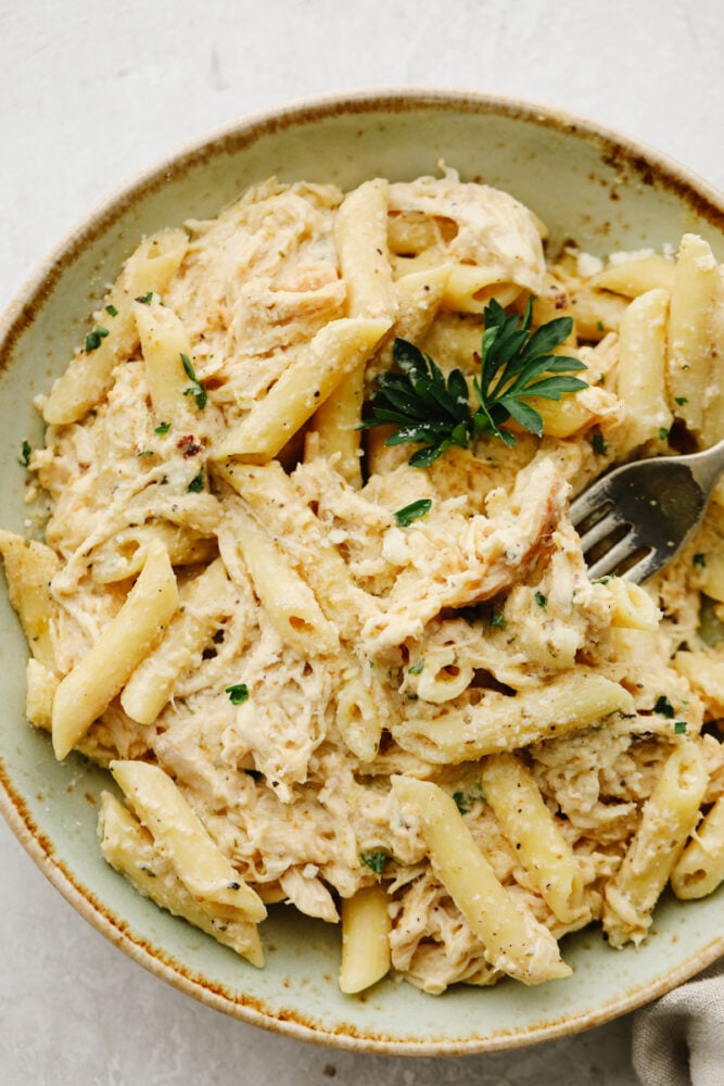 This Olive Garden crockpot chicken is to die for! The juicy and tender chicken cooked with some pasta is insanely delicious! Plus, it's super easy which is a total win-win! Chicken and pasta on a plate with a fork.