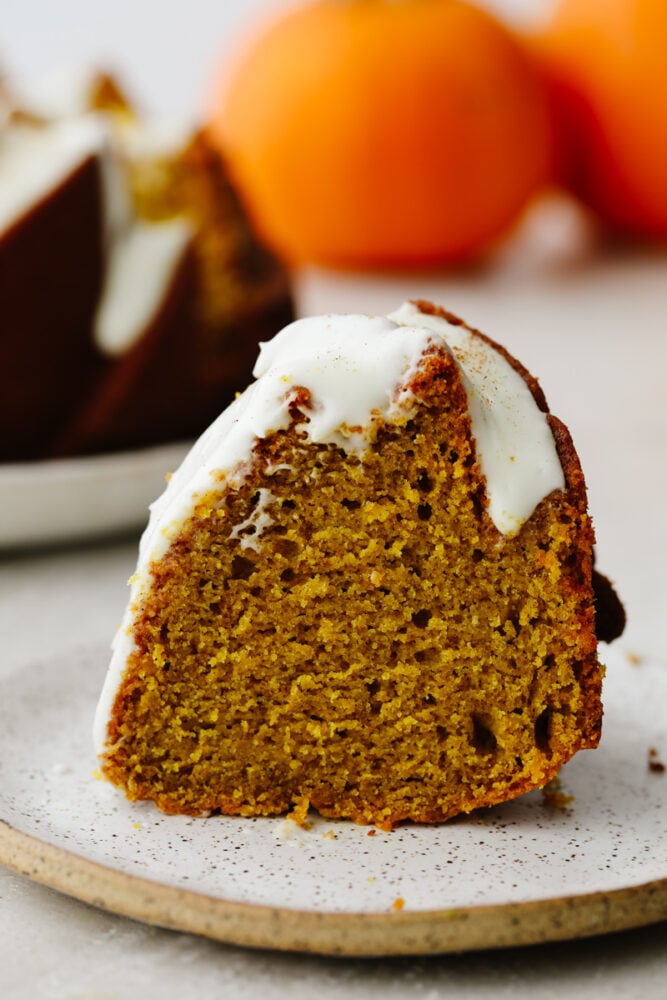 This pumpkin bundt cake with homemade cream cheese frosting is what dreams are made of! It's incredibly moist and loaded with all the pumpkin spice flavor. Slice of pumpkin bundt cake with frosting.