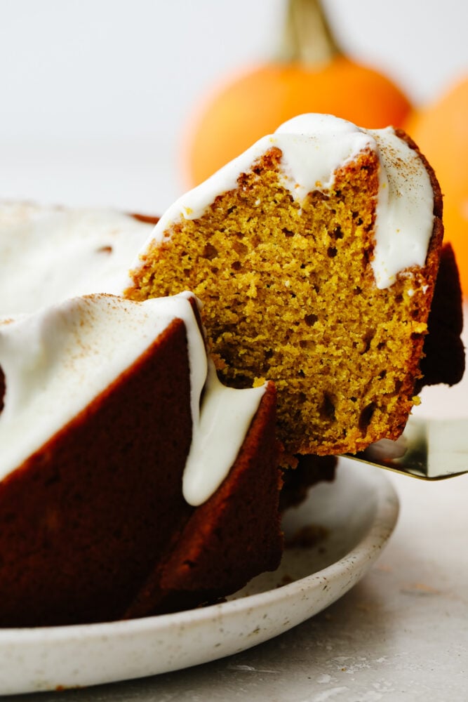 This pumpkin bundt cake with homemade cream cheese frosting is what dreams are made of! It's incredibly moist and loaded with all the pumpkin spice flavor. Pumpkin slice being pulled out of the cake.