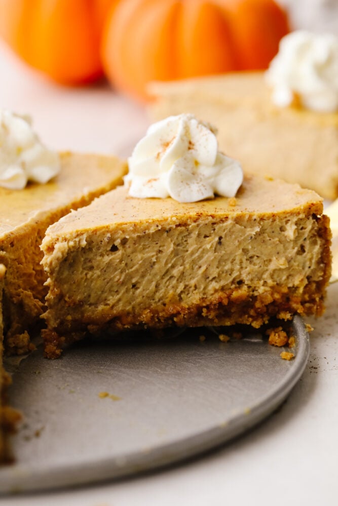 This pumpkin cheesecake that is drizzled with caramel sauce is the ultimate fall dessert. It's rich, creamy, and spiced to perfection! A side view of a slice of pumpkin cheesecake.