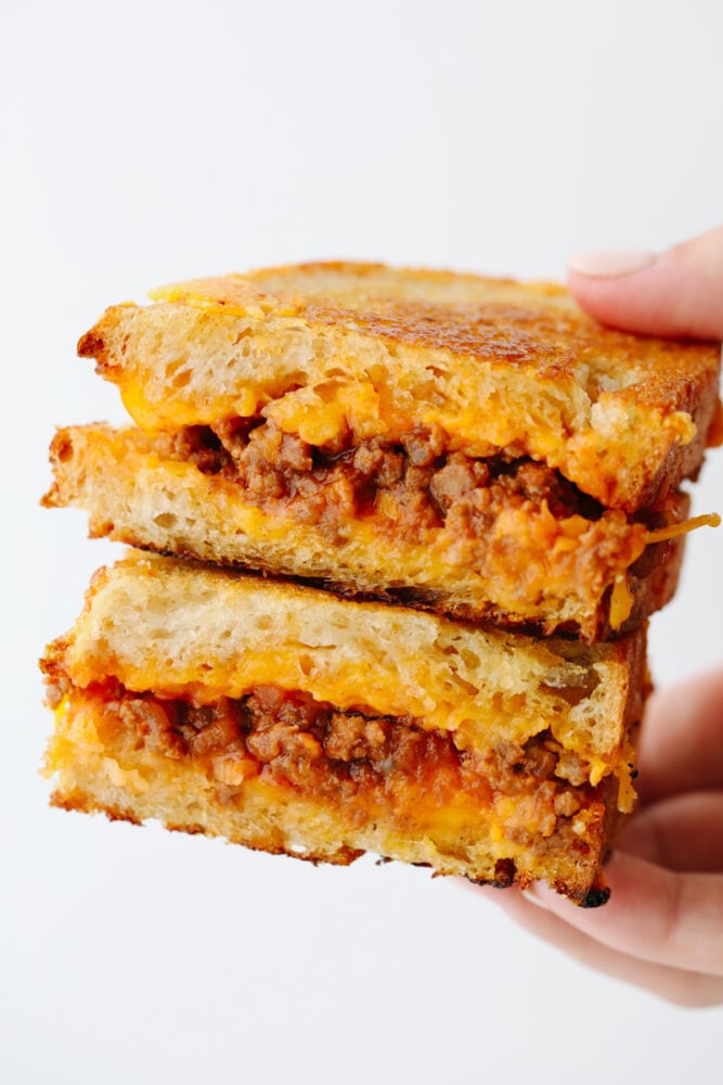 If you think a sloppy Joe grilled cheese sounds good, then just wait until you taste it! Tender, juicy and filled with flavor inside cheesy, crisped bread.. Well, it doesn't get much better than that! A hand holding 2 slices of a sloppy joe sandwich.